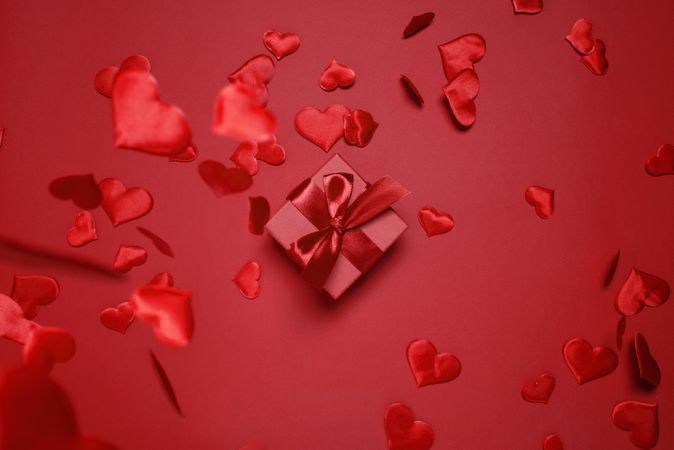 Red box with red bow on red background surrounded by falling red hearts