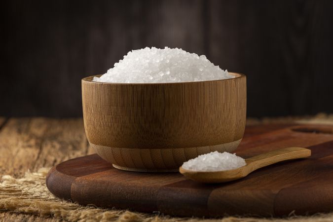 Coarse salt in bowl on wooden background.