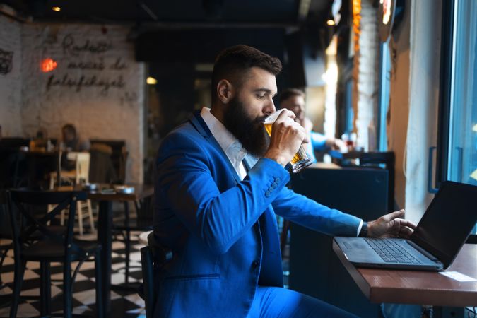 Man sipping a pint of beer in front of his laptop in a bar