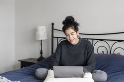 Happy young female sitting on her bed with a laptop