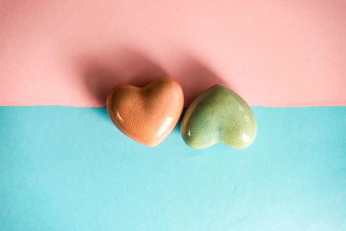 Orange and green heart ornaments on blue and pink pastel background 