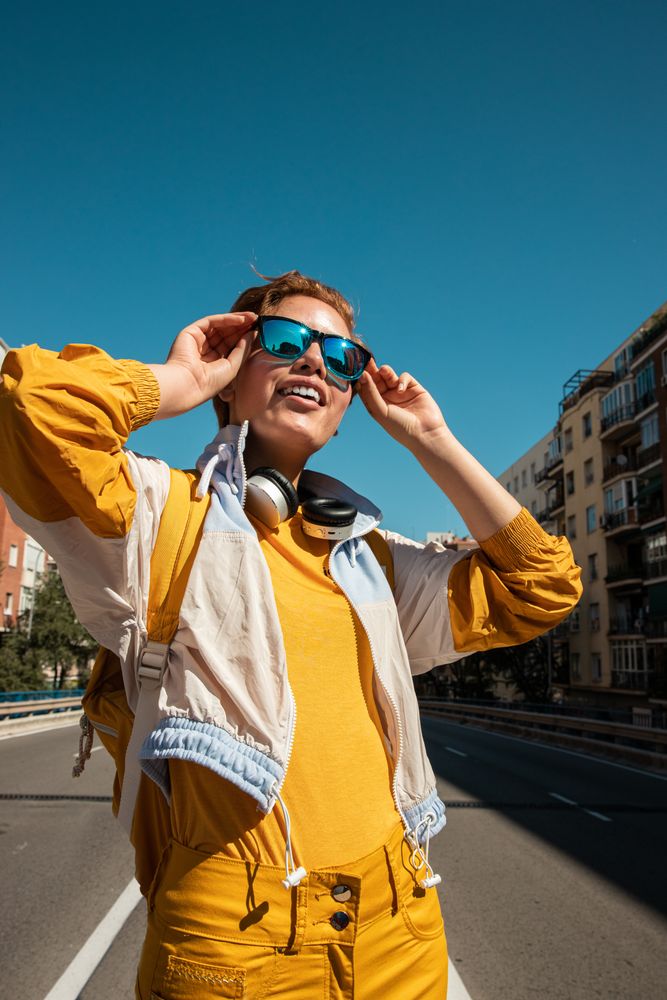 Trendy excited woman in sunglasses on street against blue sky