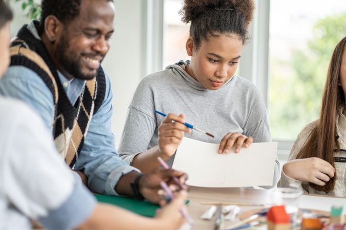 Smiling Black male teacher helping students in art class