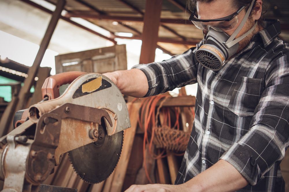 Male carpenter using electric saw cutting wood board at the carpentry workshop