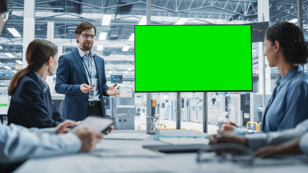 Electronics Factory Office Meeting: Male CEO Presenting Innovative High Tech Device On TV With Green Screen Chromakey.