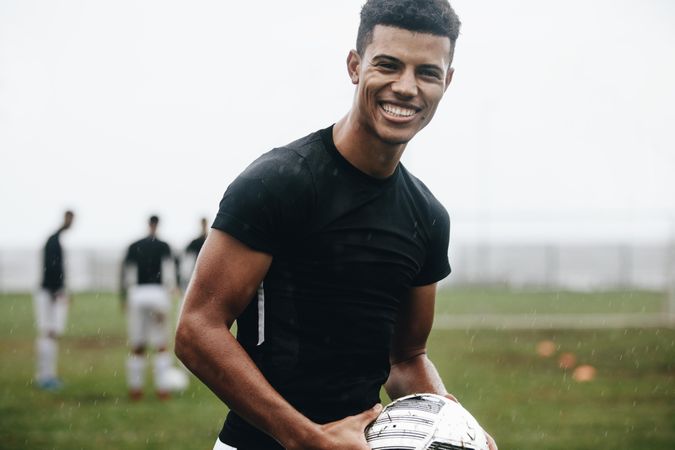 Portrait of a smiling footballer standing on field in rain