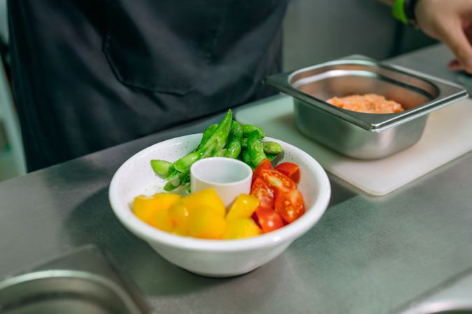 Chef is preparing poke bowl with fresh edamame, cherry tomatoes, mango fruit and salmon