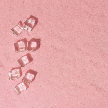 Flat lay of ice cubes on pink sand background with shadows