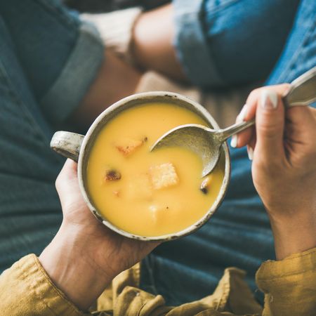 Woman in jeans holding spoon with cup of squash soup, square crop