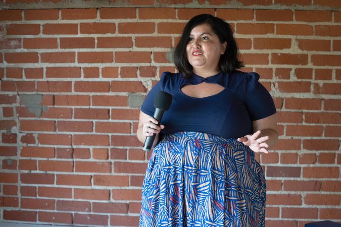 Woman giving a talk in front of a brick wall holding microphone