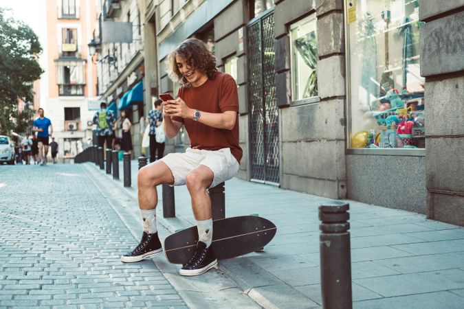 Amused man with longboard talking on phone while resting on street