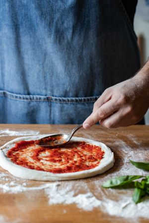 Crop man spreading sauce on pizza dough