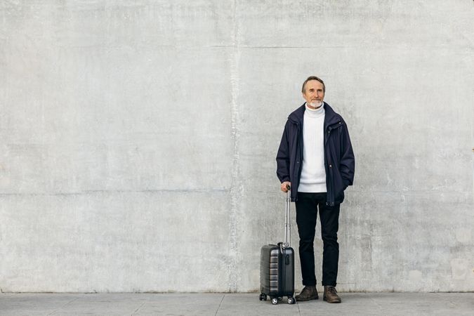 Man with suitcase outside against plain concrete wall
