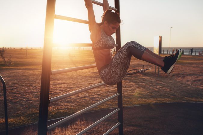 Real, healthy and fit woman performing hanging leg raises on outdoor fitness station