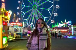Smiling young woman near illuminated ferris wheel at night