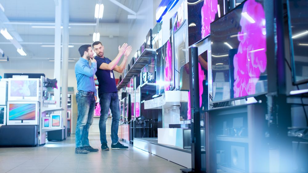 In the Electronics Store Professional Consultant Shows Latest 4K UHD TV's to a Young Man, They Talk about Specifications and What Model is Best for Young Man's Home.