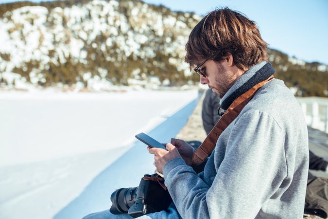 Man with cameras and phone near hill in winter