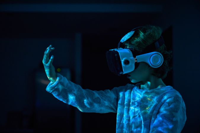 Little boy in VR goggles looking at hand in dark room