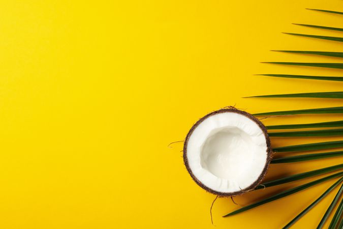 Half of coconut and palm leaf on yellow background, top view