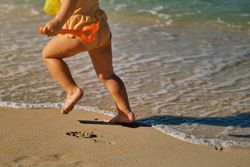 Crop girl running on sandy beach next to sea