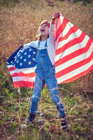Joyful boy with USA flag standing on grass