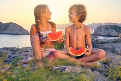 Smiling children enjoying watermelon on seashore