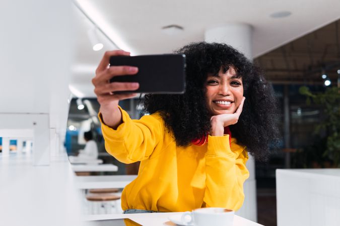 Excited young woman smiling and taking selfie in cafe