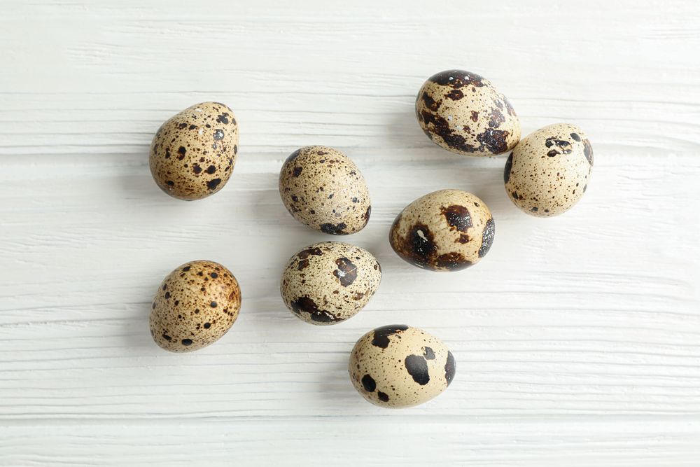Flat lay composition with quail eggs on light wooden background, space for text