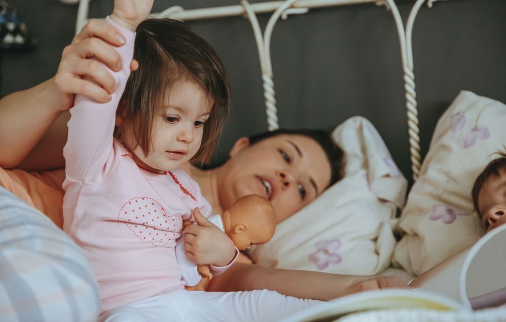 Closeup of baby reading book with her mother and brother in bed