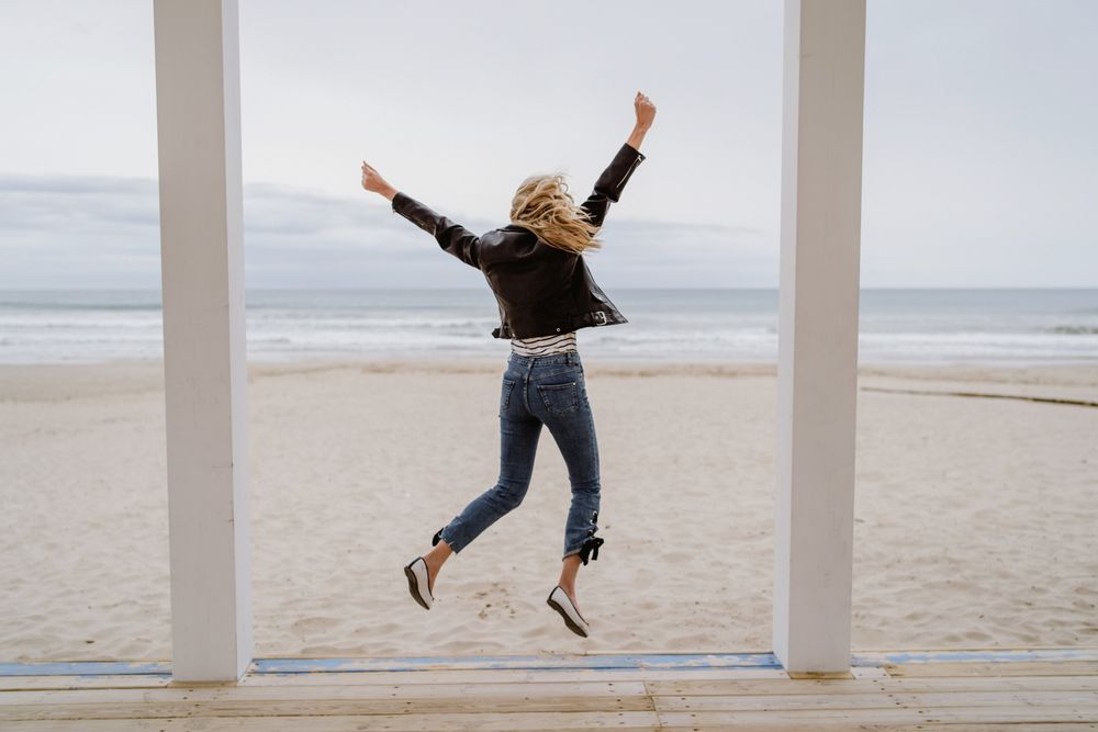 Joyful woman jumping raising hands up on wooden beach pier