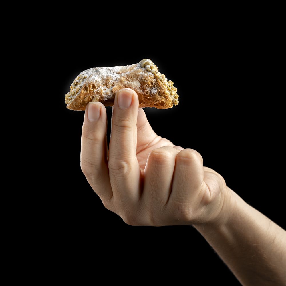 Hand holding a Sicilian cannolo on a dark background.