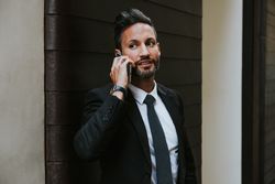 Adult stylish man in costume talking on smartphone near wall
