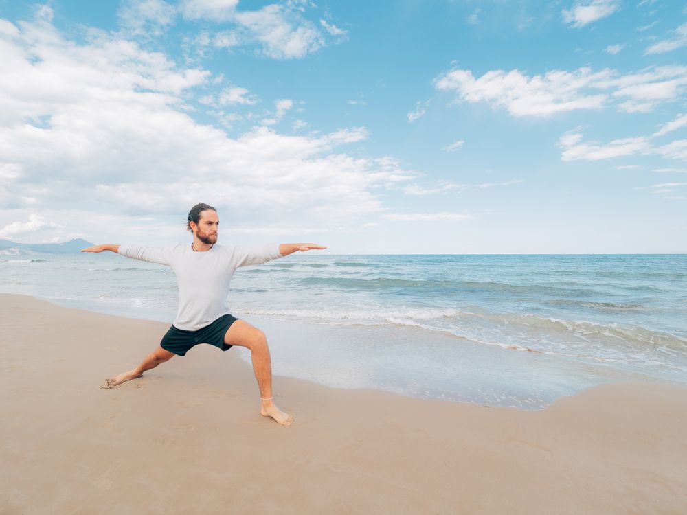 Man training yoga on beach