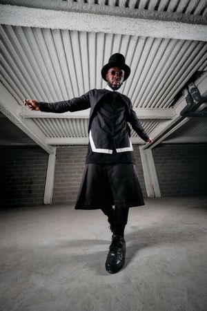 Stylish Black man in round sunglasses and hat standing in under