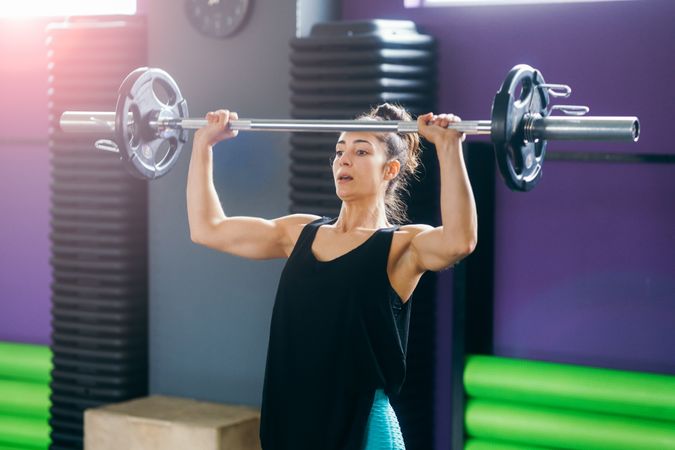 Athletic woman lifting barbell overhead in gym