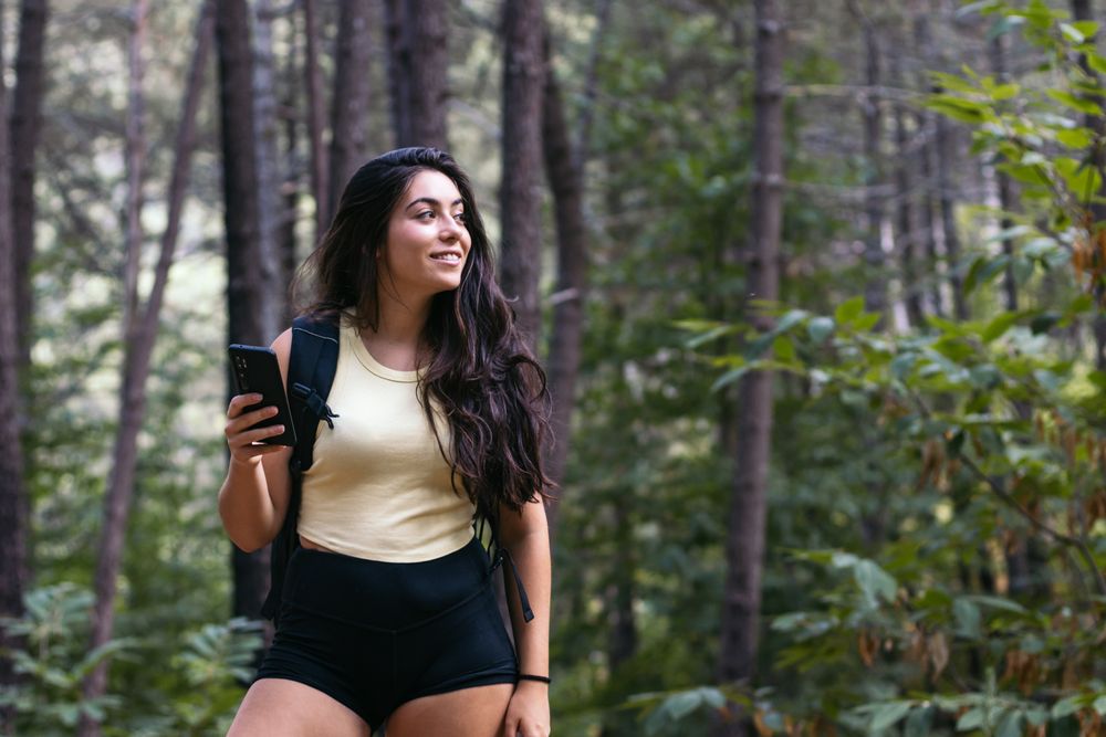 Young woman using her smartphone while hiking in the forest
