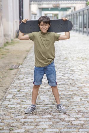 A teenage boy carrying skateboard behind head and smiling