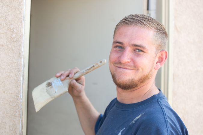 Young Man Smiling As He Is Painting House