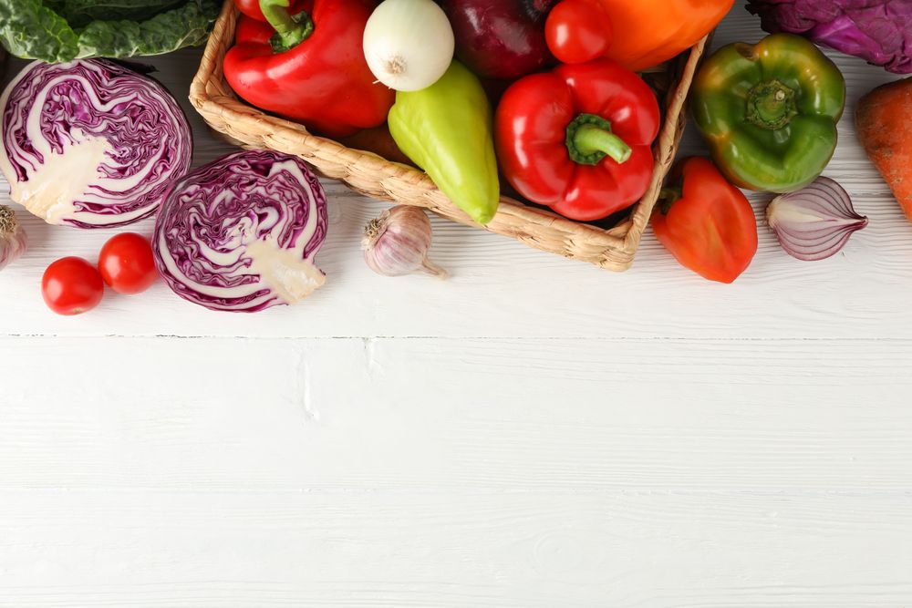 Wicker basket and vegetables on wooden background, top view