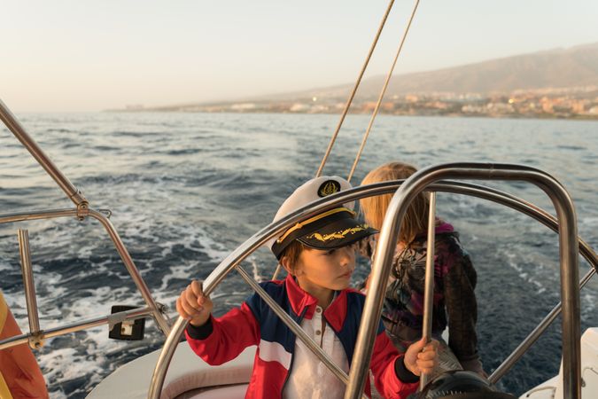 Smiling children holding steering wheel on yacht on water