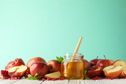 Fresh pomegranate, apples, pot of honey with dipper on mint background, copy space