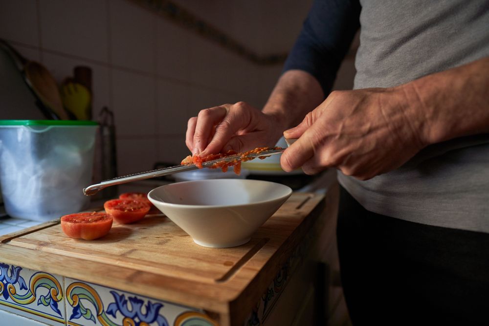 Anonymous man grating tomato into bowl