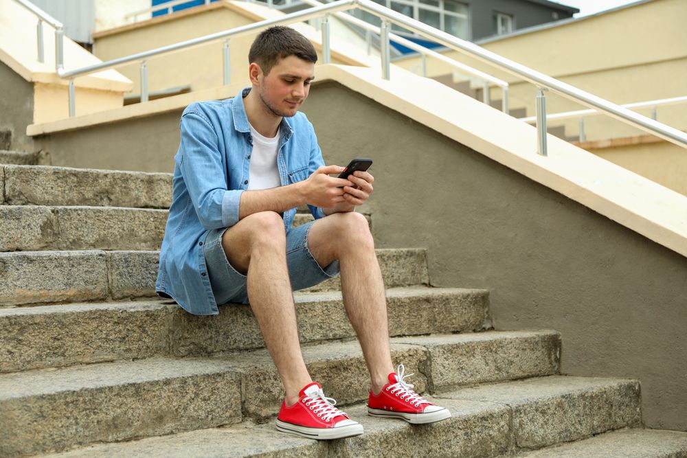 Young man sits on the steps and looking in phone