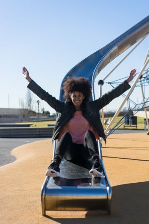 Woman with afro hair jumping down a slide.