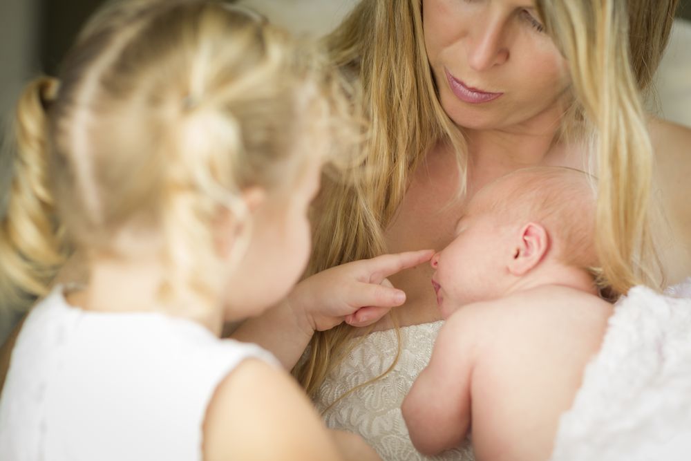 Mother Holds Newborn Baby Girl as Young Sister Looks
