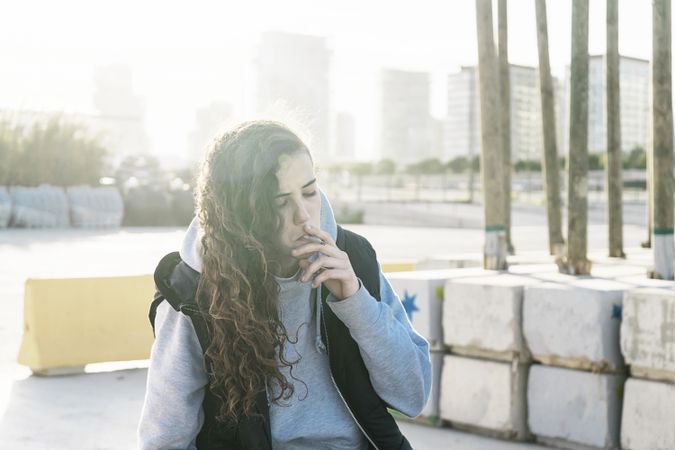 Young teenage girl sitting down and smoking outdoors