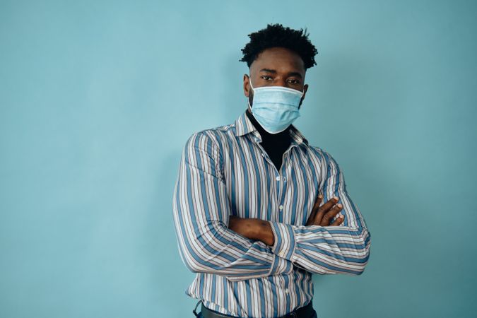 Portrait of a Black man in face mask blue studio shoot with his arms crossed