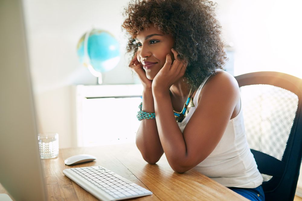 Content curly haired female at her home office desk reading computer screen