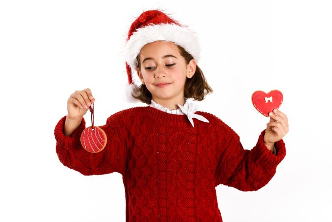 Female child in Christmas outfit holding up two decorated cookies