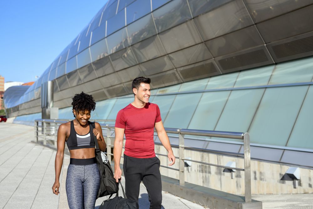 Happy sportive man and woman walking along wall in city